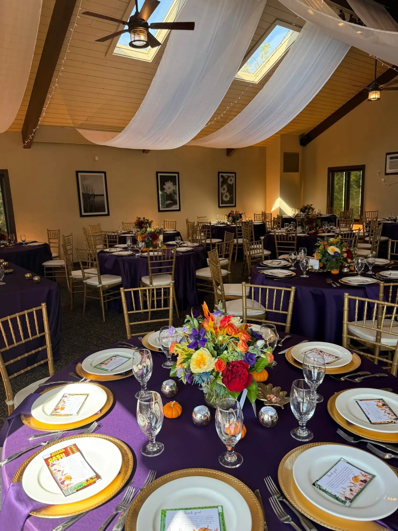 Banquet room set with purple linens, gold Chiavari chairs and colorful autumn centerpieces