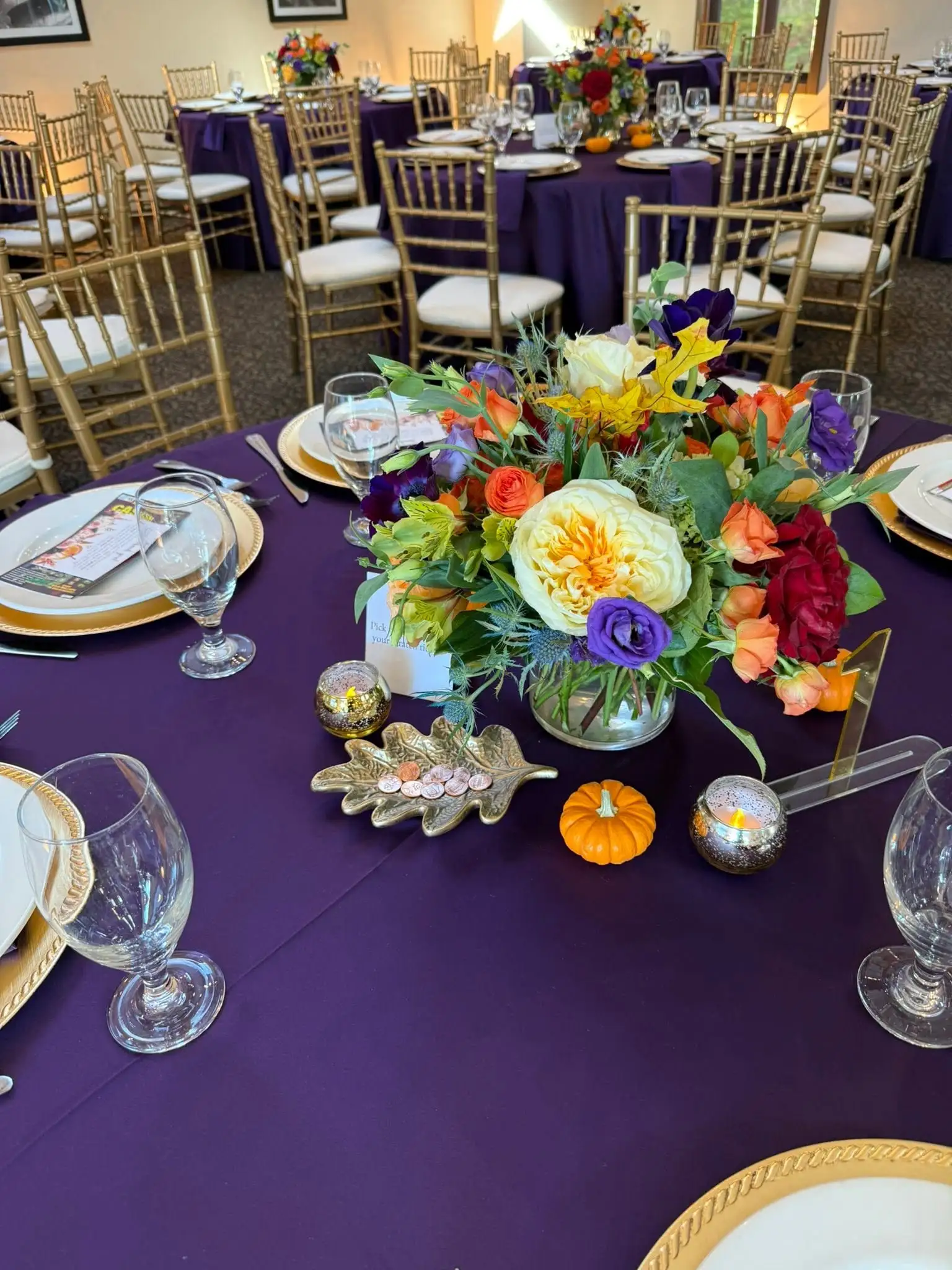 Autumn centerpiece of garden roses, thistle and mini pumpkins on a deep-purple table