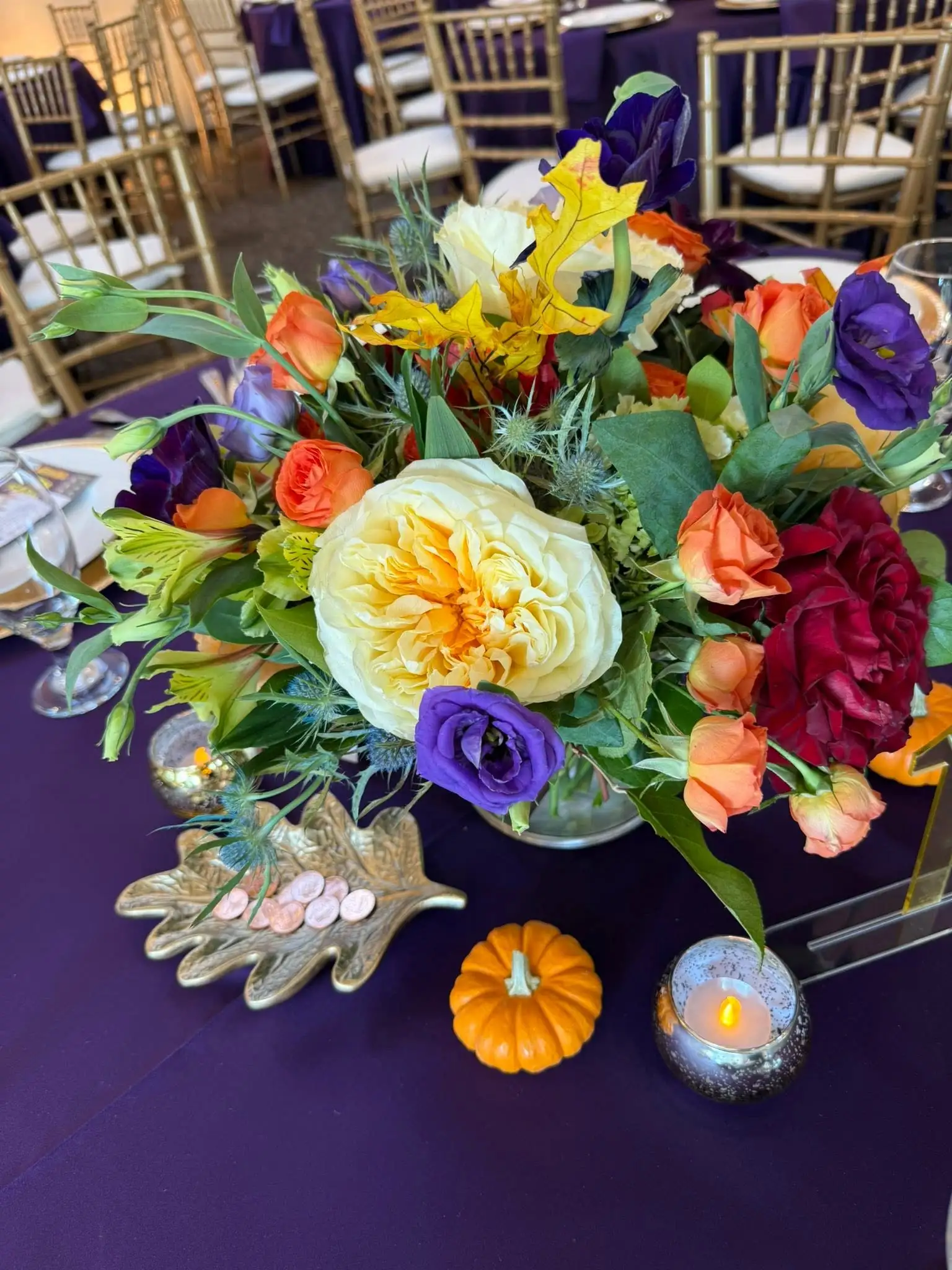 Close-up of a vibrant fall floral centerpiece with pumpkins and gold leaf accents