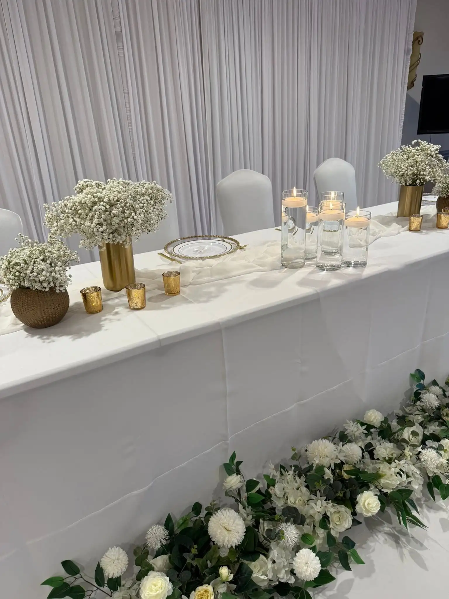 White-and-gold head table with baby's breath, floating candles and a cascading floral garland