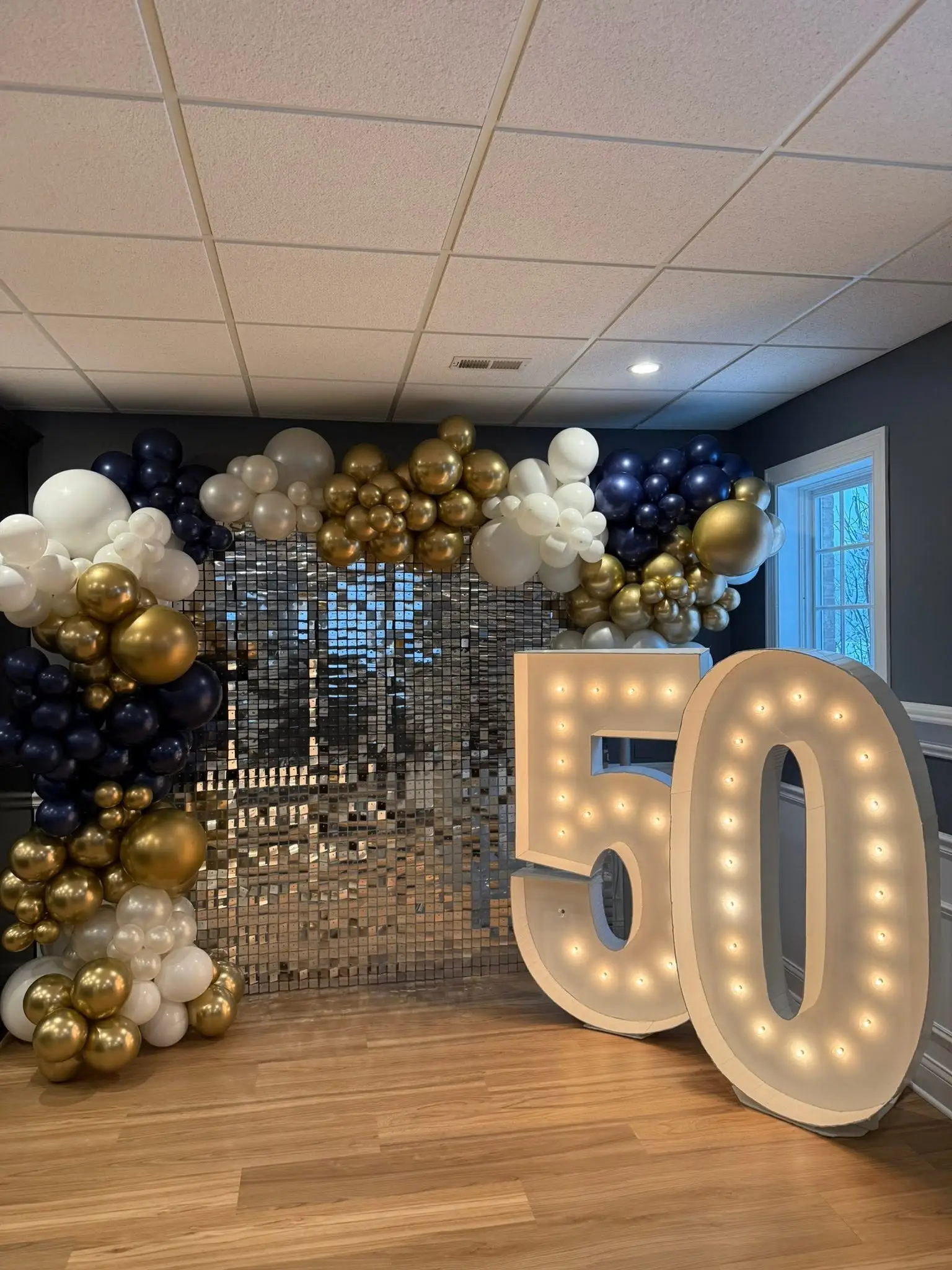 Navy, white and gold balloon garland with a light-up marquee number for a milestone celebration