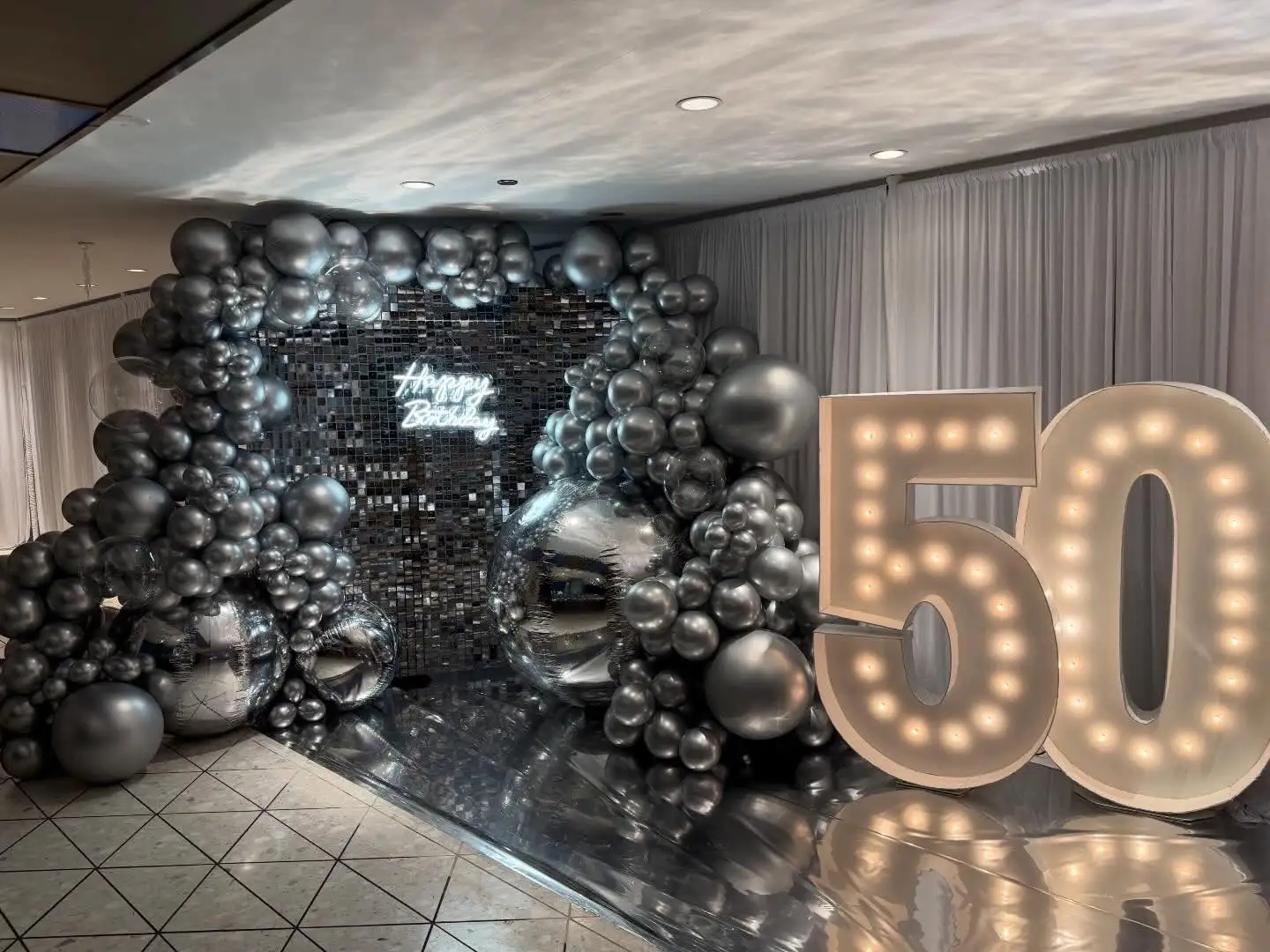 Silver chrome birthday backdrop with a mirror shimmer wall and a light-up 50 marquee