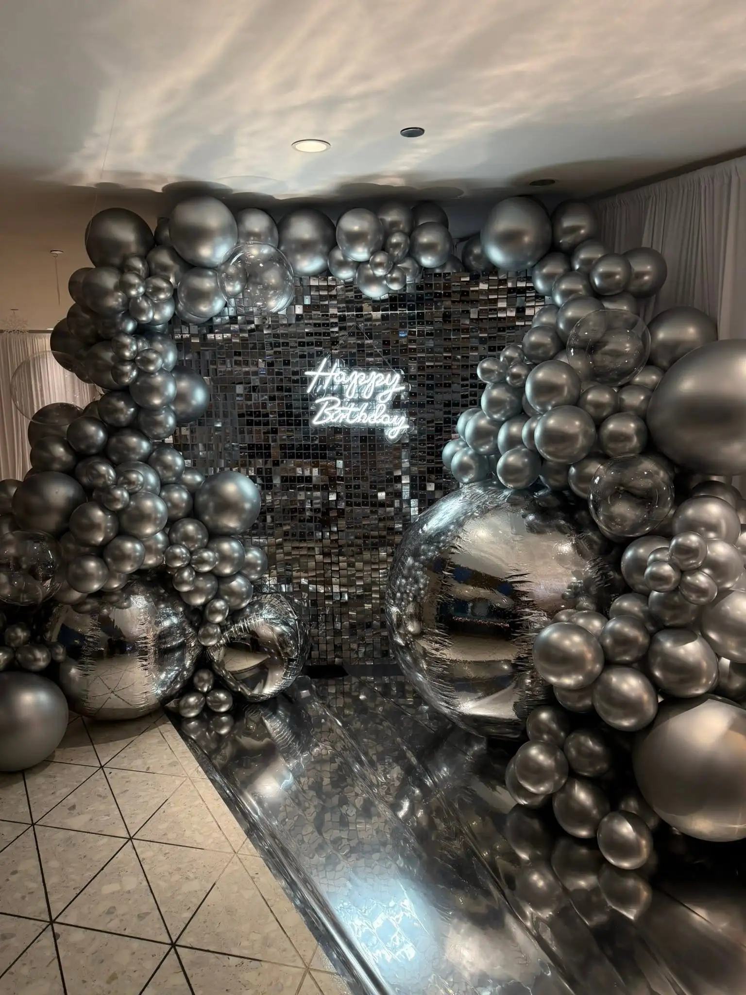Silver chrome balloon arch around a shimmer wall backdrop for a birthday celebration